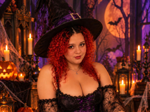 RosalieVittoria with curly red hair, wearing a black lace corset, purple bustier, and witch hat, has big tits and a cute face, surrounded by candles and Halloween decorations.