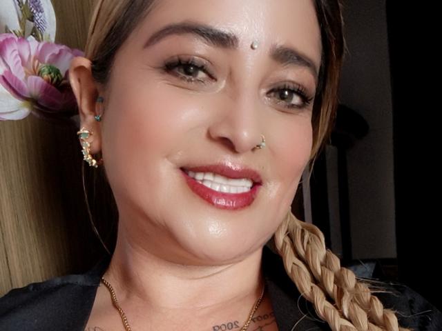 AlessadraJoness ha un viso luminoso, rossetto rosso, capelli castani intrecciati, piercing al naso e alla fronte, orecchini verdi e un sorriso che mostra denti bianchi. Indossa una maglietta nera..