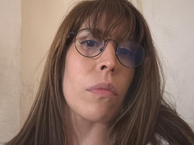 SeleneBrigth ha i capelli castani, occhiali con lenti blu e un'espressione seria. Il suo naso è dritto e indossa una camicia bianca. Le sue labbra sono leggermente serrate..