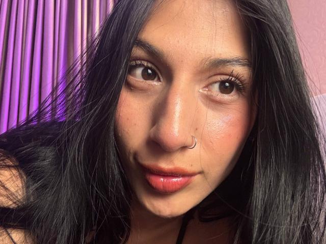 SophieBeaumont has long black hair, a nose ring, and full pink lips with a slight pout. Her brown eyes are slightly squinted. She has a light skin tone.