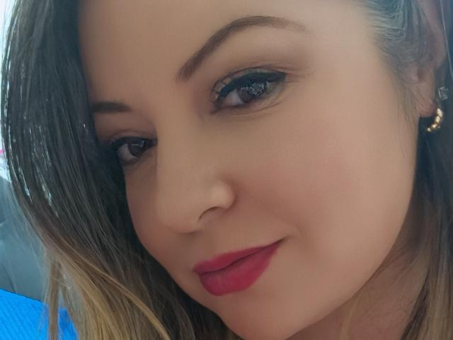 NatalyHami a un joli visage avec des yeux marron, du rouge à lèvres et des cheveux blonds avec des mèches. Elle sourit légèrement et porte une petite boucle d'oreille. Sa peau est claire et lisse..