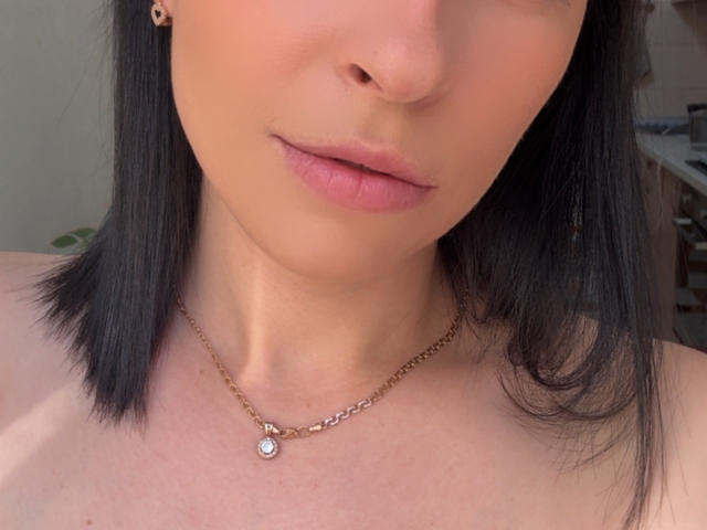 Emmas Gesicht mit schwarzem, schulterlangem Haar, rosafarbenen Lippen und heller Haut, sie trägt eine kleine goldene Kette mit einem Diamantanhänger, wobei ihr Oberkörper zu sehen ist..
