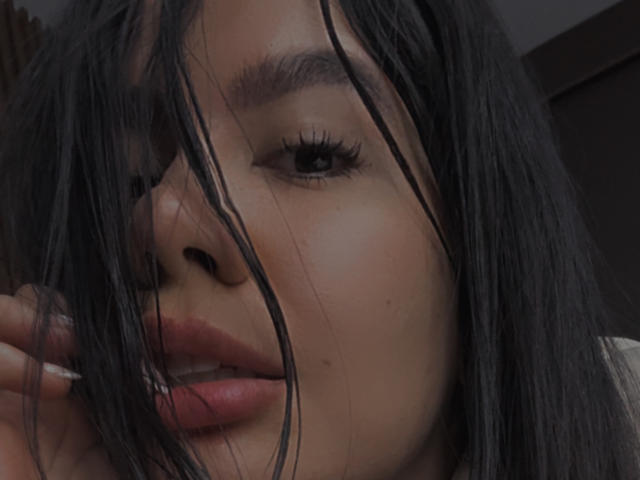 Le visage de Valentina Eliott, avec ses longs cheveux noirs qui lui cachent les yeux, ses lèvres roses légèrement entrouvertes et ses cils visibles, dégage une impression de douceur, de naturel et d'un certain désordre..