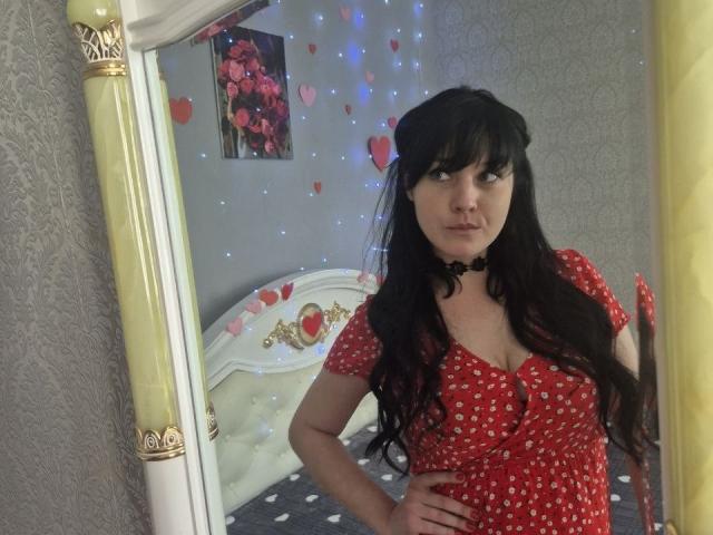 WenTina with long black hair, wearing a red polka dot dress, black choker, standing in front of a mirror, hands on hips, looking at camera, showing her tits.