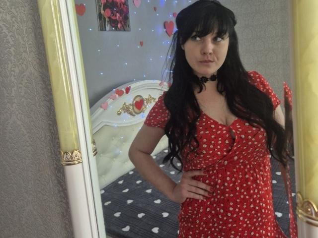WenTina with long black hair, wearing a red dress with white polka dots, black choker, and standing in front of a mirror, showing off her small tits.