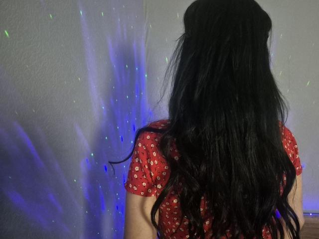 WenTina with long, wavy black hair, wearing a red shirt with white patterns, standing with her back to the camera, illuminated by blue and purple lights.