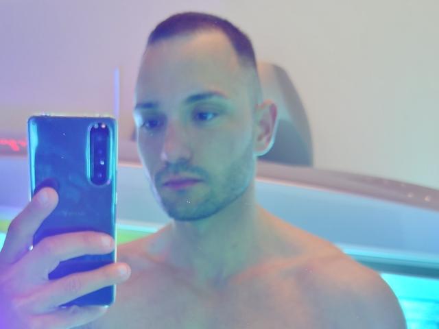 Ein obdachloser Twunki mit Kurzhaarschnitt, der ein Selfie in einem unscharfen, farbenfrohen Bild macht, ein schwarzes Telefon in der Hand hält, ernst aussieht und blaue und violette Lichtreflexionen zeigt..