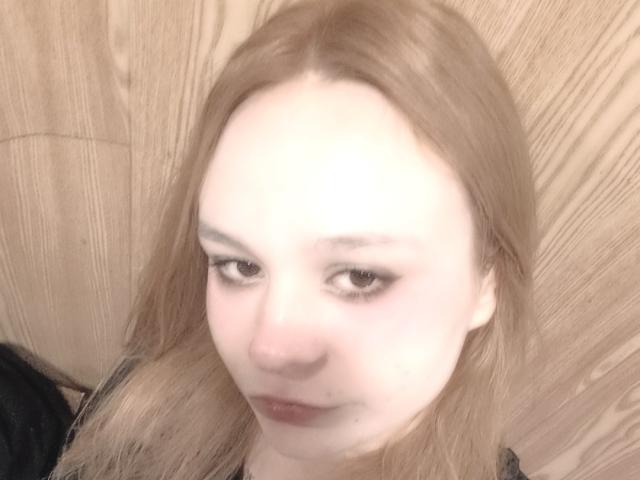 JanelSavala's face with light brown hair, pale skin, and half-lidded brown eyes, looking slightly down with a subtle, relaxed expression. Her nose is small, lips are slightly parted.