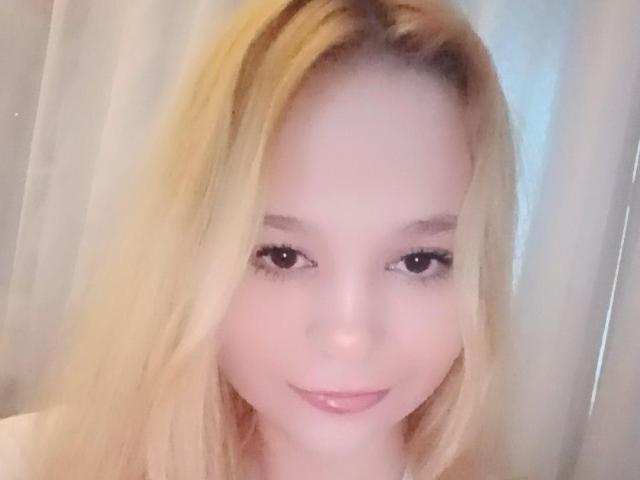 JanelSavala with blonde hair, fair skin, and pink lips, smiling at the camera with subtle makeup, showing her cute face and small nose. Her ass is not visible.