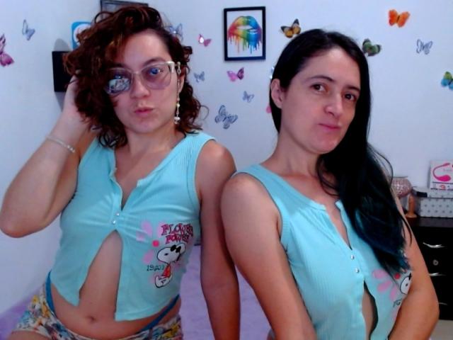 LunaVenus with curly brown hair and glasses on left, wearing a blue top with cutout and floral pants, stands next to LunaVenus with black hair, blue top, and no pants.