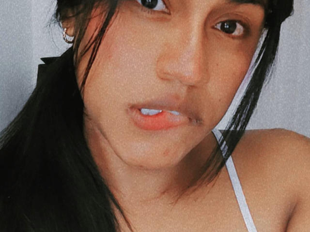 IvannaDuran69 tem um rosto atraente, com cabelo preto, olhos castanhos e pasta de dente branca em seus lábios levemente entreabertos. Ela está vestindo uma blusa branca com alças finas..