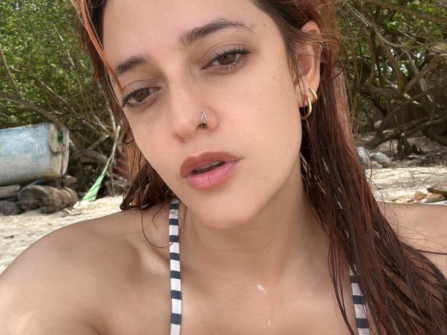 JaneRoa has brown eyes, a nose piercing, and gold hoop earrings. She's wearing a striped halter top, with wet brown hair and a slightly open mouth.