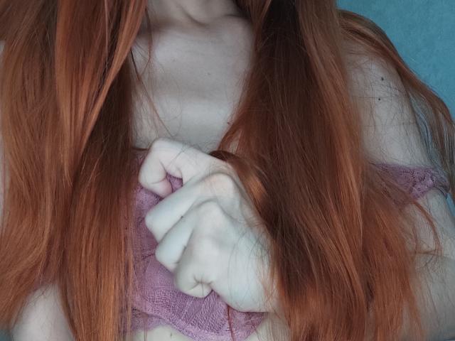 SheritaChieng's red hair covers her pale skin, gripping a purple lace bralette, exposing her small, white tits with her hand. Her fingers are slightly curled, showing a gentle grip.