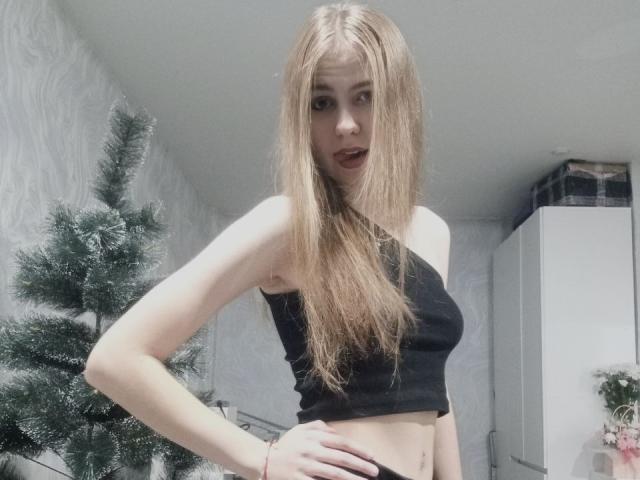 MargretWarriner with long blonde hair, black crop top, showing her small tits, hand on hip, looking at camera, standing in front of a decorated Christmas tree.