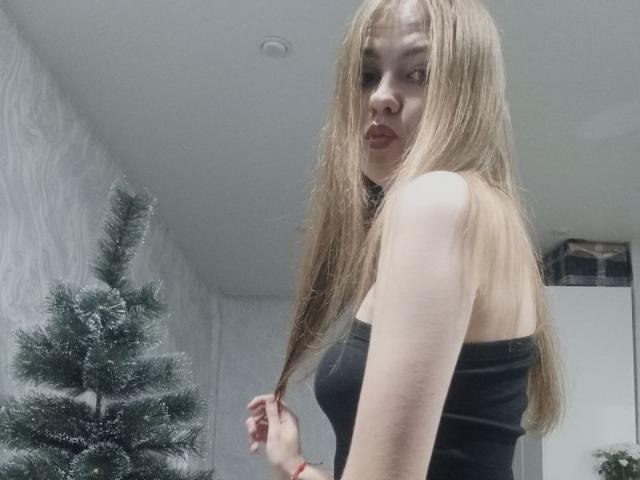 MargretWarriner with long blonde hair, pouty lips, black strapless top, looking over shoulder, holding hair, small tits, fair skin, standing by a decorated Christmas tree.