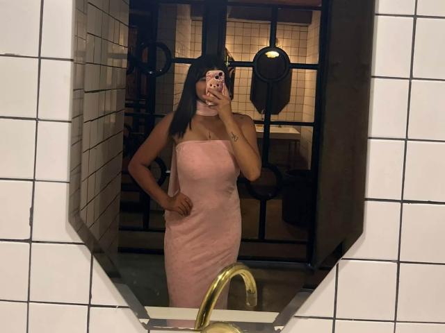 AshlyLee with dark hair in a pink, strapless, bodycon dress, standing in a tiled bathroom, taking a mirror selfie, showing her tan skin and small ass.