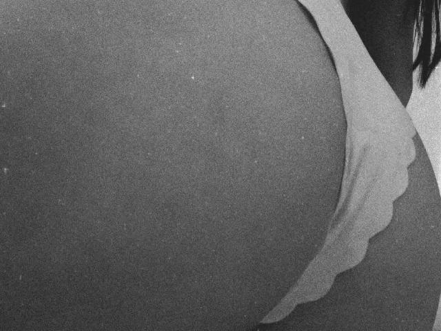 CherryBuchel's ass in a tight, sheer, white garment with a wavy edge, partially revealing her dark skin. Black and white, grainy texture, emphasizing the curvature.