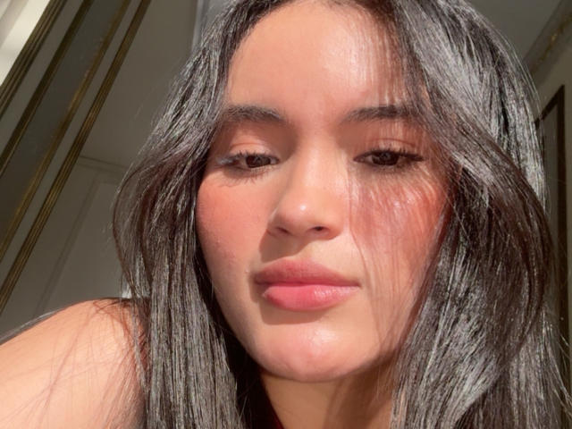 MiiaPalmer has long, straight black hair, slightly flushed cheeks, and pink lips. Her brown eyes are half-closed, and she's looking down with a subtle, confident smile.