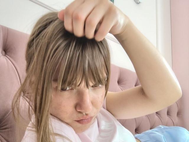 SondraCanestrini has a sweaty face, pulling her brown hair with a clenched hand, eyes closed, wearing a white shirt, on a pink tufted couch.
