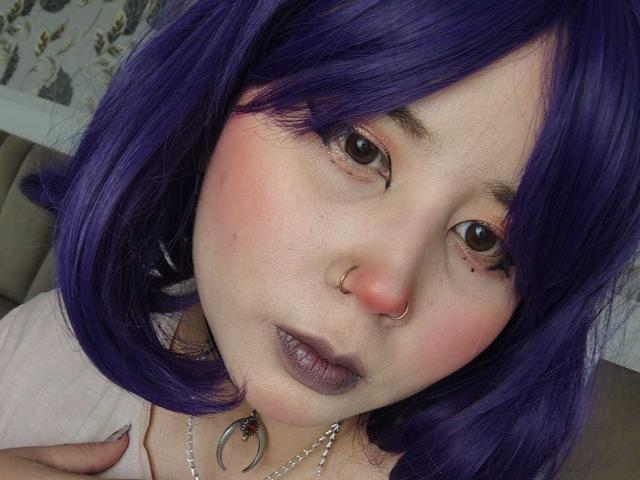 WendyMonet with purple hair, nose ring, and purple lipstick, has pink cheeks, brown eyes, and a silver necklace with a crescent moon, looking at the camera.