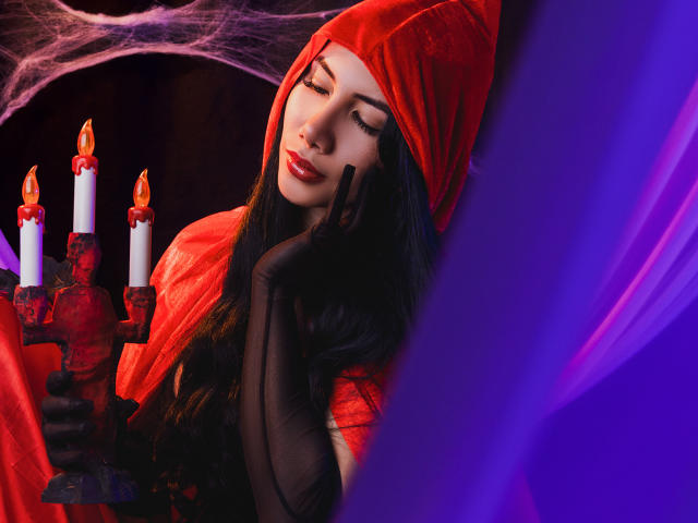 ArianaRogers in a red hood, black gloves, holding a red candelabrum with lit candles, eyes closed, red lips, long black hair, purple and red lighting, sexy.