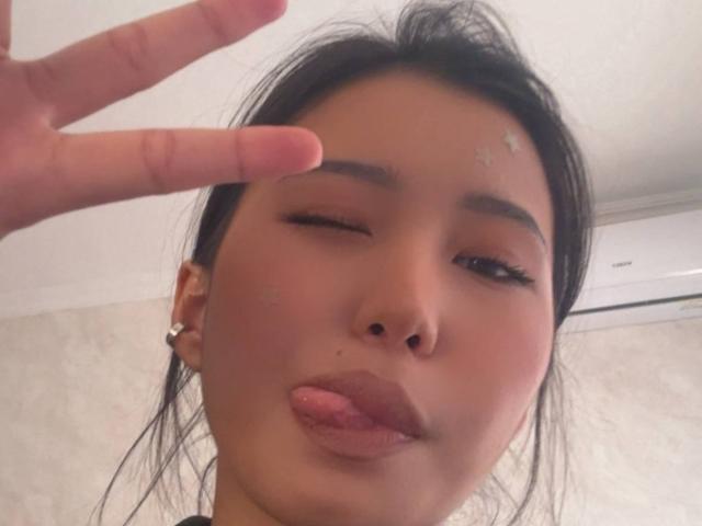 LeonilaSeewald has dark hair, brown skin, and is winking with her tongue out, making a peace sign with her right hand. She has small acne scars on her forehead.