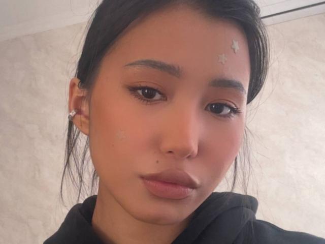 LeonilaSeewald has light brown skin, black hair, and small star-shaped acne marks on her forehead. She's wearing a black hoodie and diamond earrings, looking slightly bored.