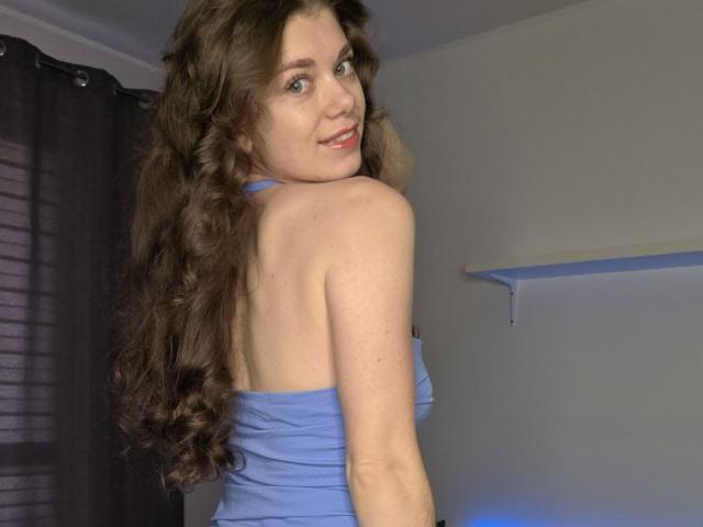 YourRedFlag has long brown curly hair, wearing a blue strapless top, looking over her shoulder with a slight smile, showing her back and ass.