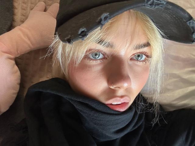 Arnetta Nazario, con i capelli biondi, gli occhi azzurri e un cappello nero con un segno di usura, indossa una felpa nera e ha una mano vicino alla testa, guardando verso l'alto con le labbra leggermente dischiuse..