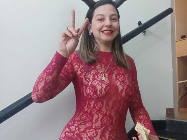 ArianaBlonde with medium tits, wearing a red lace dress, black bunny ears, smiling, holding a yellow napkin, and flashing a peace sign with her right hand.