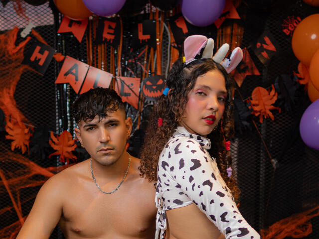 ElkynAndNell with curly brown hair, bunny ears, and white spotted shirt, next to shirtless ElkynAndNell with dark hair, looking at camera, in Halloween-themed photo.