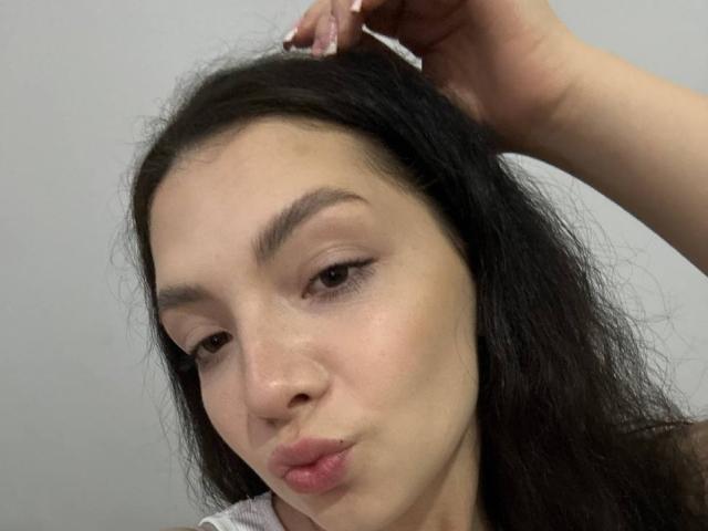 Cristal Erickson, con labios carnosos, ojos marrones y cabello negro, se está subiendo el pelo con la mano derecha. Tiene un tono de piel claro y está haciendo una mueca..