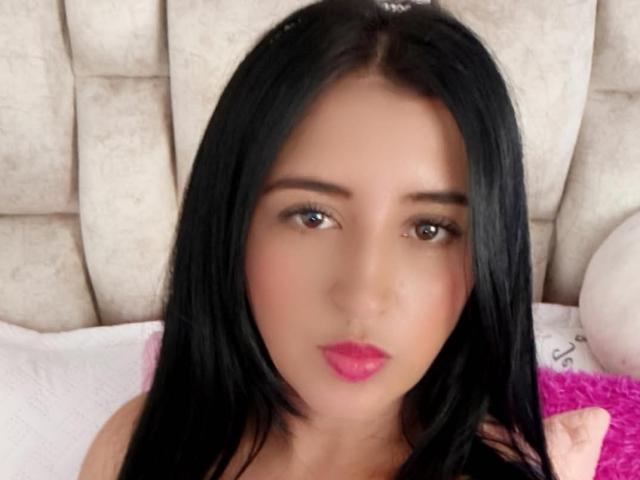 NicollJeans has straight black hair, brown eyes, pink lipstick, and a neutral expression. She's looking directly at the camera with a subtle, serious face.