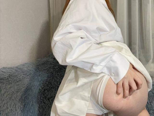 LilliamChevalier with white shirt covering her tits, white underwear pulled down to expose her ass, hand gripping her butt, sitting on a blue fuzzy pillow.