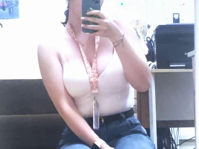 Ellaria with small tits in a white sleeveless top, pink lanyard, and blue jeans, taking a mirror selfie. Her arm is slightly raised, showing a black watch.