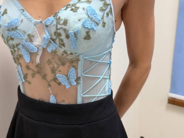 Rorria's sheer, light blue top with embroidered blue butterfly and green leaf patterns, lace-up sides, and black skirt, showing her tits through the fabric.