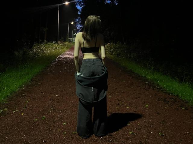 ShanekaKonig stands on a dark path at night, holding down black pants, wearing a black bra, exposing her ass, with her back to the camera, under streetlights.