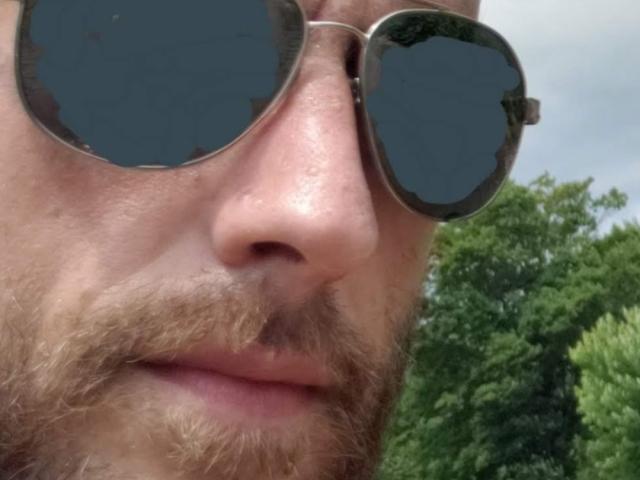 MenMadisonYes has a beard, circular sunglasses with dark lenses, and a slightly sweaty nose. His face is close to the camera.