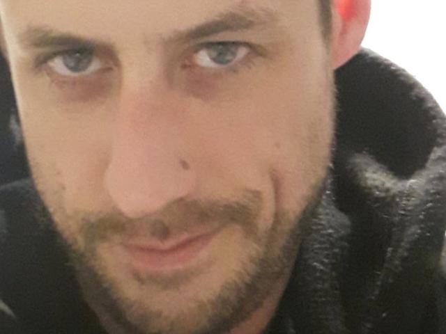 MenMadisonYes has a slightly bruised nose, light brown beard, and a small mustache, with a subtle smirk, wearing a black hoodie, and has blue eyes and light skin.