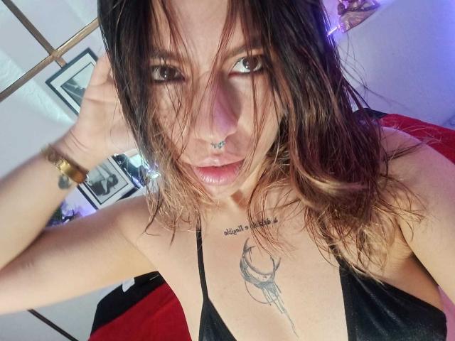 DulceBom with wet, dark brown hair, black nose ring, and black tattoo above her tits, wearing a black top, looking at the camera with a slightly parted lip.