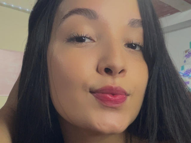 SarahGood has a cute face with brown skin, black straight hair, raised eyebrows, and pink lipstick. She's pouting her small ass. Her eyelashes are long and dark.