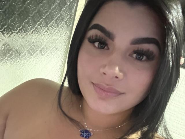 AntonellaBellas has medium brown skin, long black hair, thick eyebrows, big eyelashes, and is smiling with light pink lips. She's wearing a blue pendant necklace.