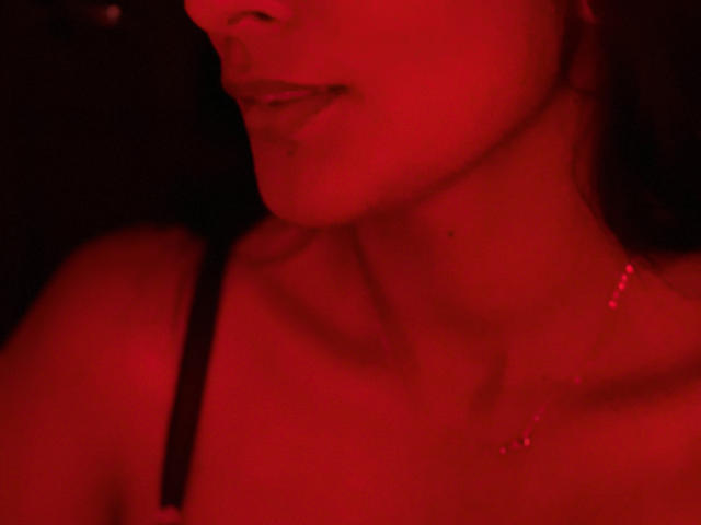 AmeliRoux's red-lit face, showing her lips and part of her neck with a small mole. She's wearing a black strap and a delicate necklace. Red lighting.