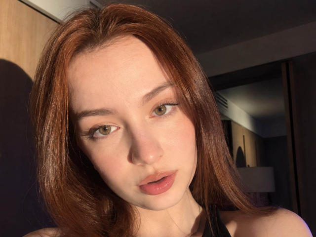 AlissaMencia ha la pelle chiara, gli occhi verdi e i capelli castano-rossicci, con labbra piene di colore rosa e un sorriso appena accennato, indossa un top nero con spalline, sotto una luce solare intensa..