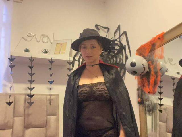 GianineLarose with dark lace lingerie, black sheer robe, and witch hat, standing in a room, black choker, small tits, medium ass, blonde hair, white walls, and a soccer ball.