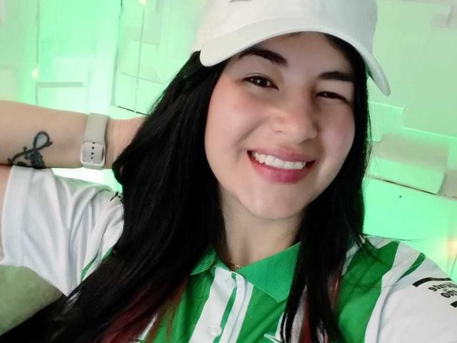 NinaHarpper with black hair, white cap, green and white soccer shirt, smiling, winking, wearing a smartwatch, has a tattoo on her left arm. Her tits are not visible.