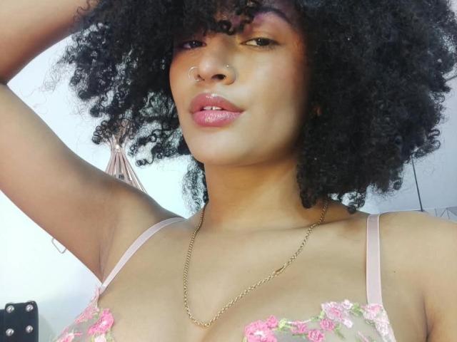 SnackTime a les cheveux noirs et bouclés, un piercing au nez et des lèvres roses brillantes. Elle porte un soutien-gorge en dentelle rose et une chaîne en or. Ses seins sont petits et visibles..
