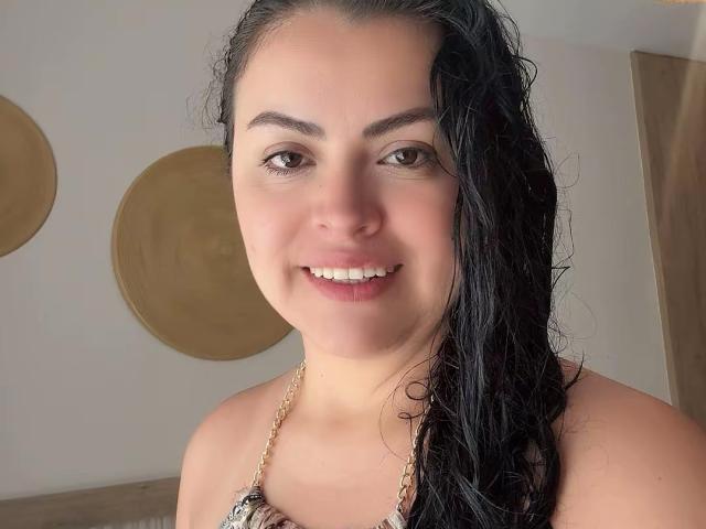 Charlotte Devereaux, con i capelli neri bagnati, sorride, mostrando i denti, e indossa un top a fascia con perline. Le sue natiche non sono visibili, il suo seno è piccolo ed è coperto dal top..