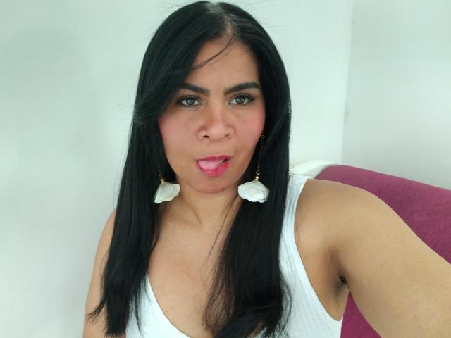 Rhouss has long black hair, wearing a white tank top, with small white flower earrings, sticking her tongue out, showing armpit hair, and has medium-sized tits.