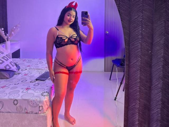 Arianna Dolche aparece en un selfie frente al espejo, vistiendo lencería de encaje negro, una liga roja y cuernos de diablo rojos. Tiene un cuerpo curvilíneo y sexy, con senos grandes y redondeados y un trasero prominente..